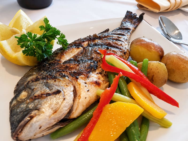 A whole grilled fish with potatoes, green beans, peppers and lemon
