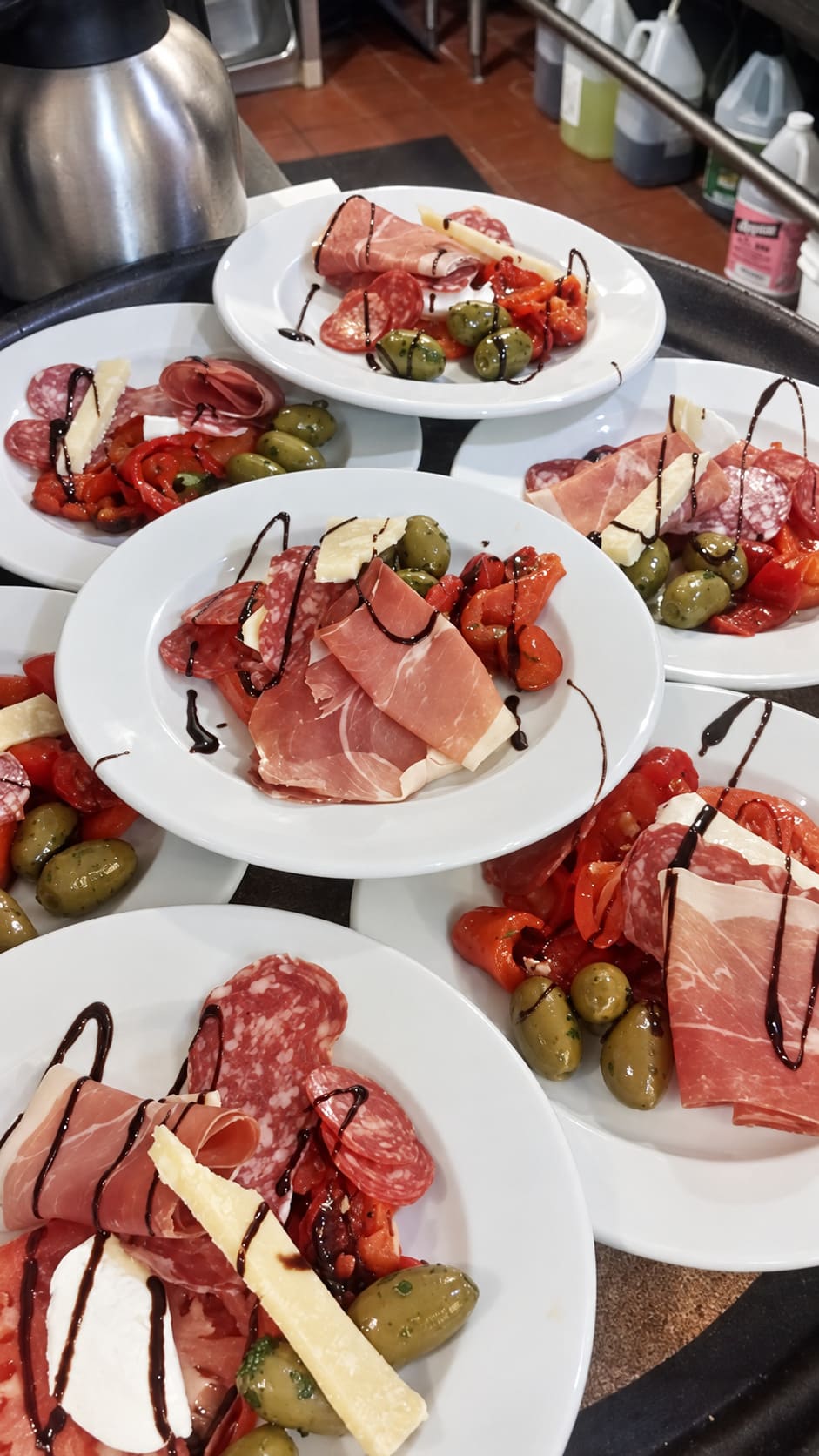 Antipasto plates of cured meats, olives, roasted peppers and cheese lined up for service